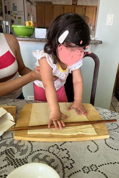 My toddler using a rolling pin to roll out dough as she beings her cooking with toddlers era