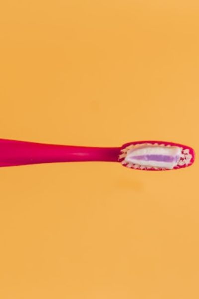 red toothbrush with some toothpaste on it on an orange background