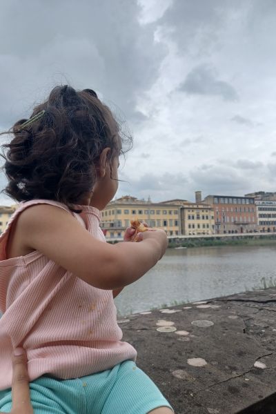 my daughter enjoying a croissant on a bridge in Florence. she's looking at the water